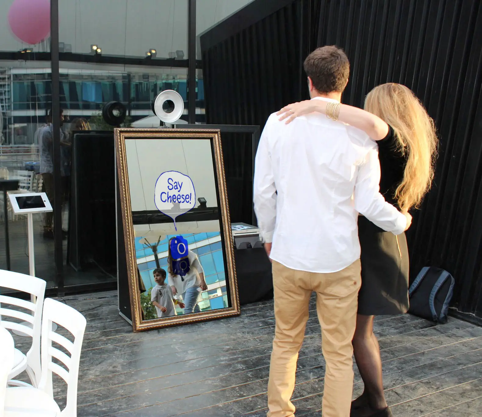 A reflection of a couple posing in front of the Parti-Panorama Photo Booth with the playful words "Say Cheese" displayed on the mirror at a family event