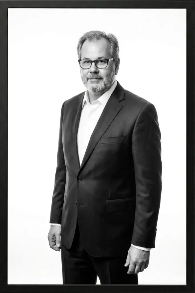 A man posing in front of a camera in a suit, showing his profile from the lower body up