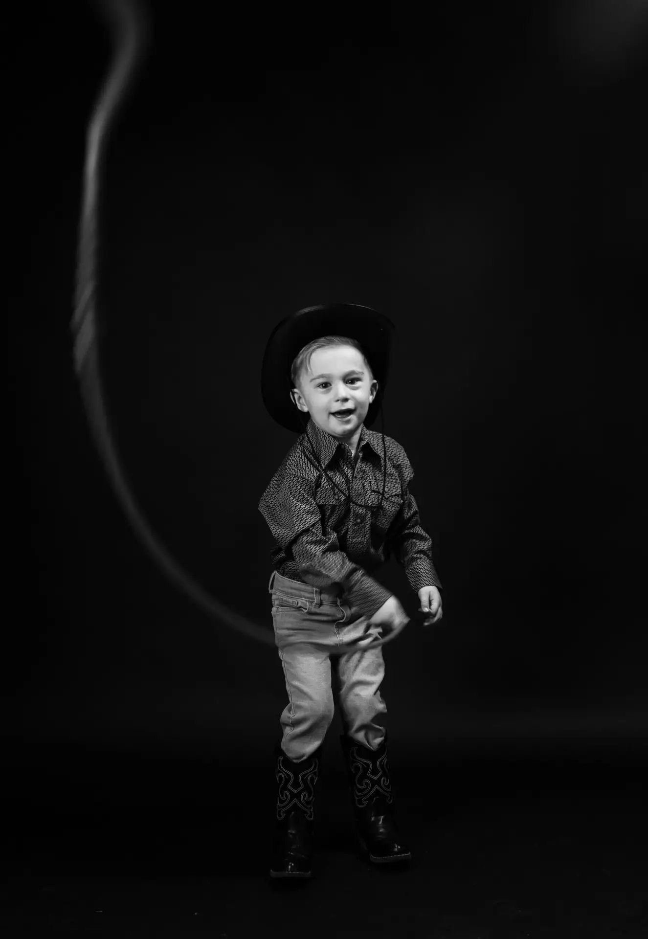 A young boy wearing a cowboy outfit posing and throwing a lasso