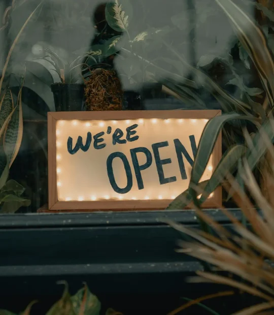 A shop grand opening with a sign saying "We're Open" in the windowsill